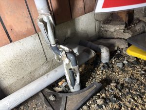 駐車スペースの外壁下で折れてしまった配管の様子。地面近くで破損している。